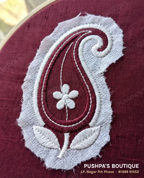 The back of machine embroidery: white stabiliser backing torn away around the motif and even white bobbin thread down the middle of each satin column