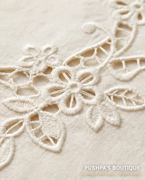 Close-up of machine cutwork on ivory cotton: flowers and leaves with dense satin-stitch edges and the cloth cut away inside, like lace