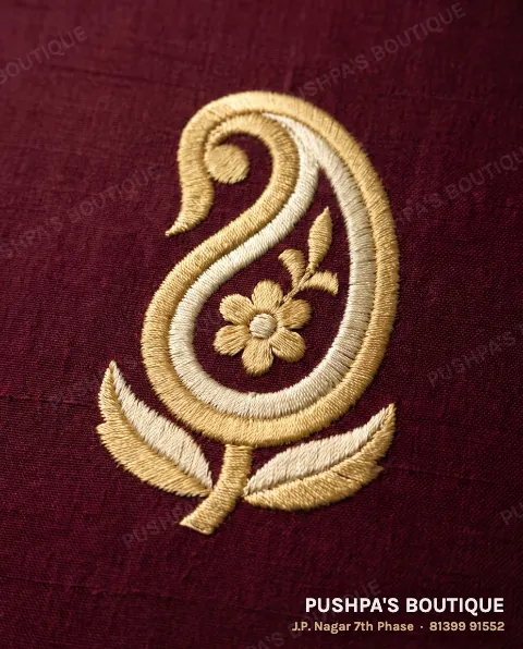 Close-up of machine embroidery: the same paisley in dense, even gold and ivory satin stitch on maroon silk, flat and smooth