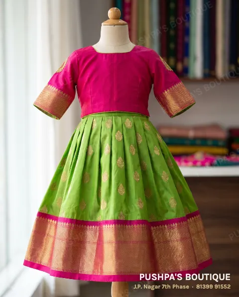 Girl's parrot-green pattu pavadai with gold buttas, a rani-pink zari border and a rani-pink blouse